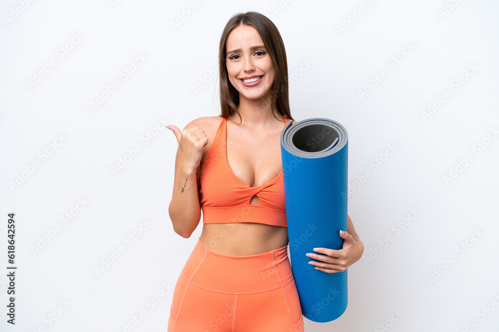 Young beautiful sport woman going to yoga classes while holding a mat isolated on white background pointing to the side to present a product Young beautiful sport woman going to yoga classes while holding a mat isolated on white background pointing to the side to present a product