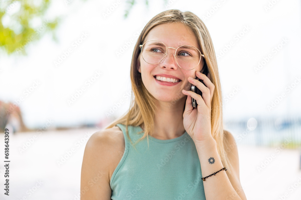 Young blonde woman at outdoors keeping a conversation with the mobile phone with someone