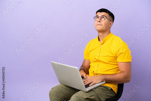 Young man sitting on a chair with laptop and looking up