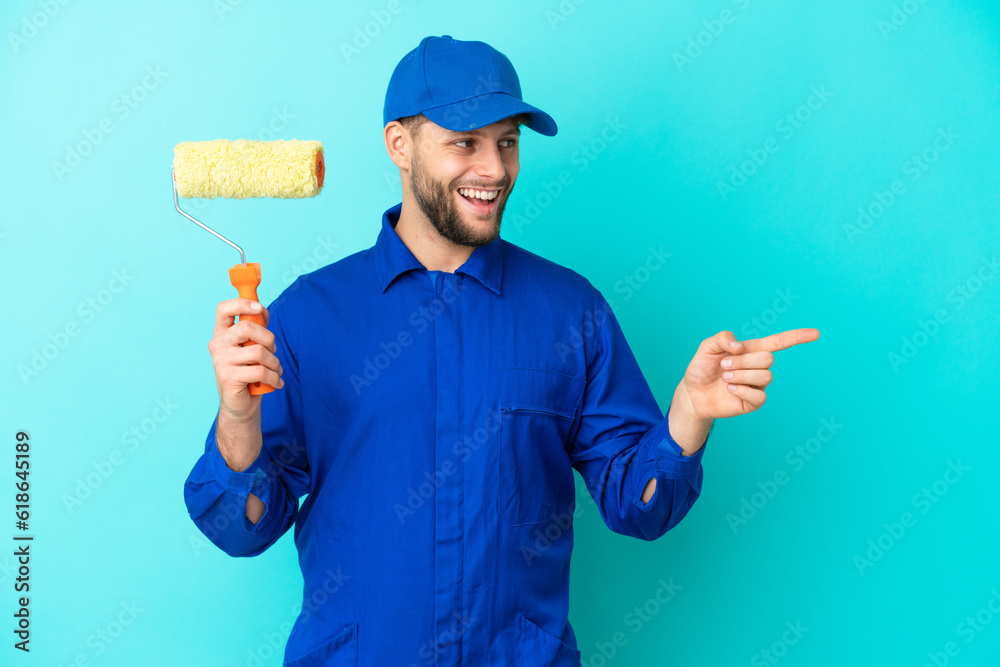 Painter caucasian man isolated on blue background pointing finger to the side and presenting a product