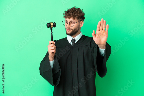 Judge over isolated green background making stop gesture and disappointed