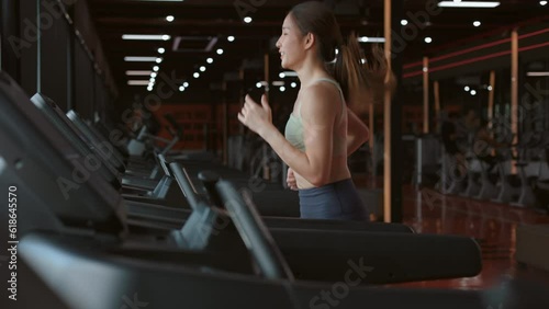 Slow motion side view filling the energy of a happy Asian woman on a gym treadmill. This captivating video inspires an active lifestyle and healthy living.