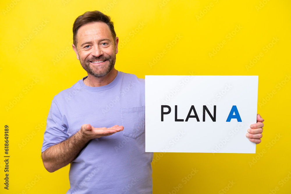 Middle age caucasian man isolated on yellow background holding a placard with the message PLAN A and pointing it Middle age caucasian man isolated on yellow background holding a placard with the message PLAN A and pointing it