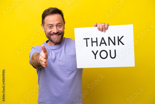 Middle age caucasian man isolated on yellow background holding a placard with text THANK YOU making a deal © luismolinero