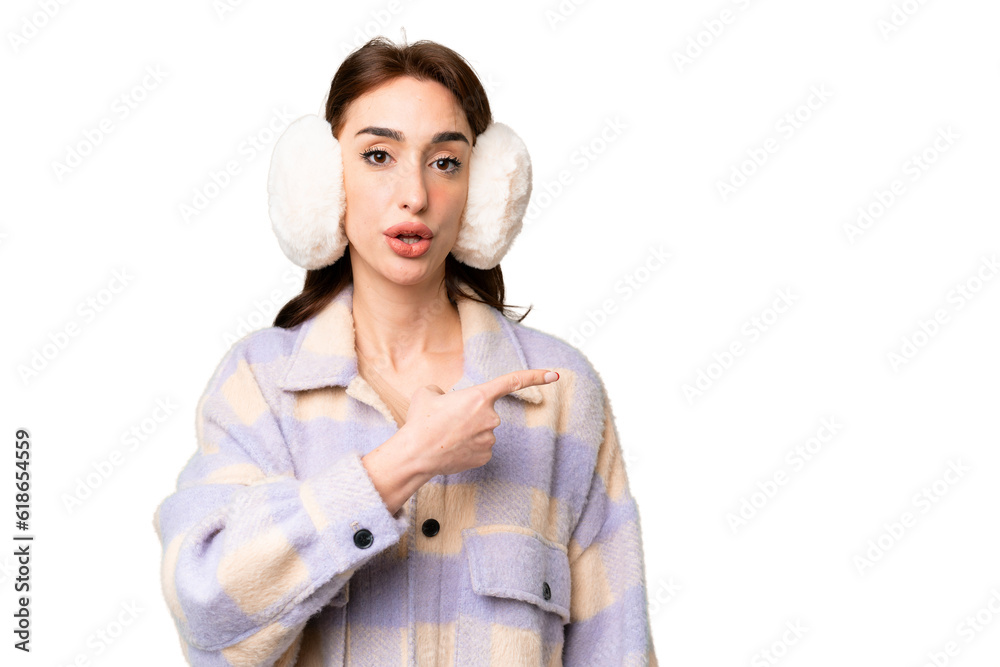 Young caucasian woman wearing winter muffs over isolated chroma key background surprised and pointing side Young caucasian woman wearing winter muffs over isolated chroma key background surprised and pointing side