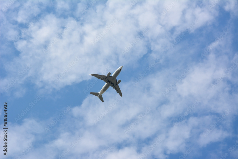 Twin engine passenger plane high in blue sky with clouds. View from below