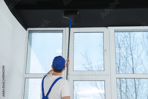 Worker in uniform painting ceiling with roller indoors