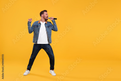 Handsome man with microphone singing on yellow background. Space for text photo