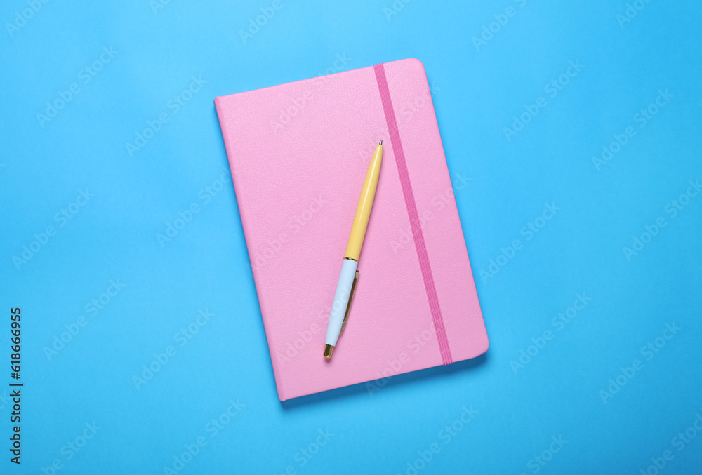 Closed pink notebook and pen on light blue background, top view Closed pink notebook and pen on light blue background, top view