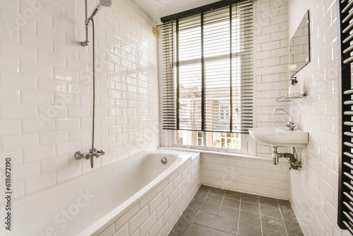 a white bathroom with black and white tiles on the floor  tub  shower  and window in the background