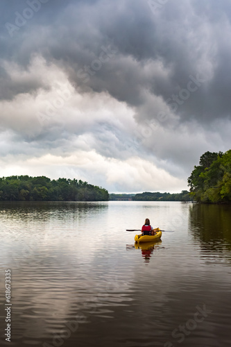 A woman paddles a yellow kayak alone on the Catawba River in North Carolina while storm clouds gather in the distance photo