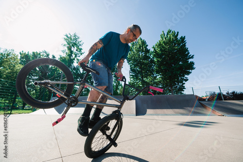 An urban oldish guy is doing a 360 rotation trick on his bmx in a skate park.