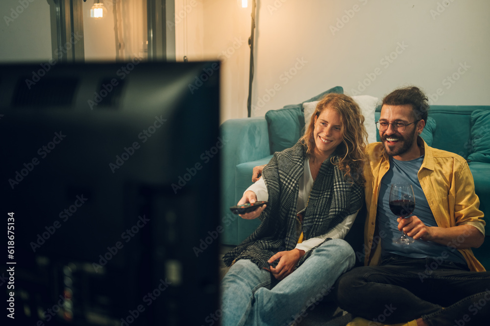 Happy couple sitting on the floor in front of the TV enjoying and drinking wine.