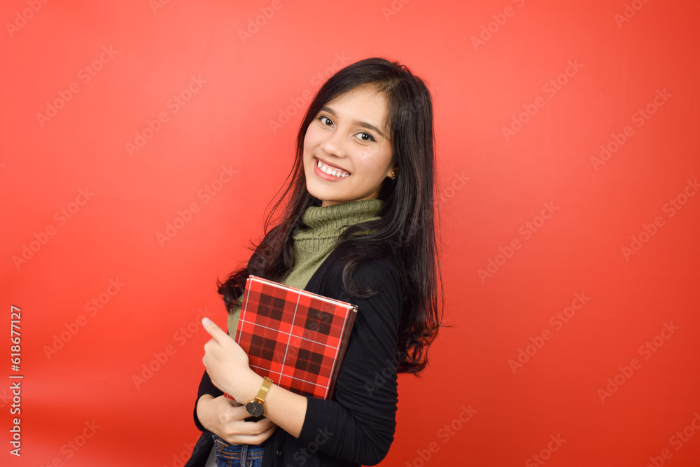 Holding Book and Smiling looking at camera Of Beautiful Asian Woman Isolated On Red Background