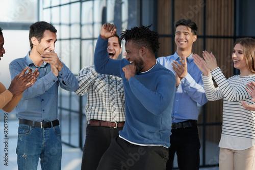 Overjoyed diverse businesspeople triumph have fun dancing in modern office corridor,