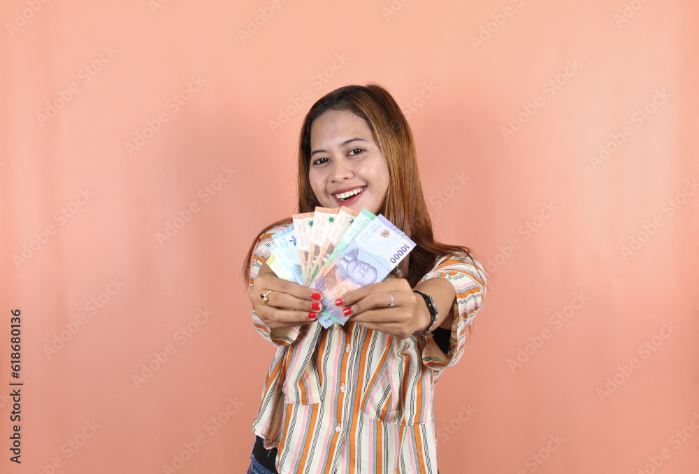 Portrait of happy Indonesian Muslim woman holding rupiah money isolated over peach background. Portrait of happy Indonesian Muslim woman holding rupiah money isolated over peach background.