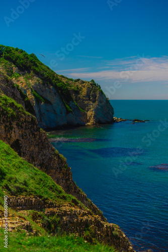 Rocks with green grass by sea on summer sunny day © Mirrorstudio
