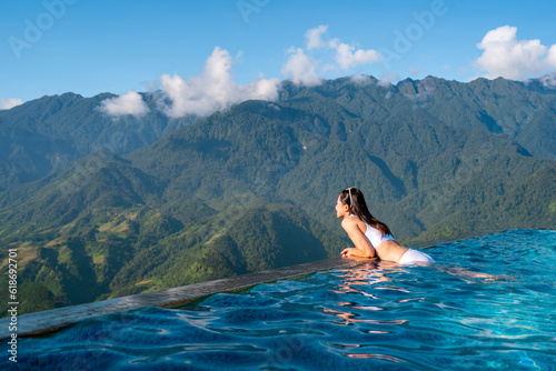 Young woman traveler relaxing in sky pool and looking at the beautiful nature landscape with blue sky and mountains in Sapa, Vietnam © Kittiphan