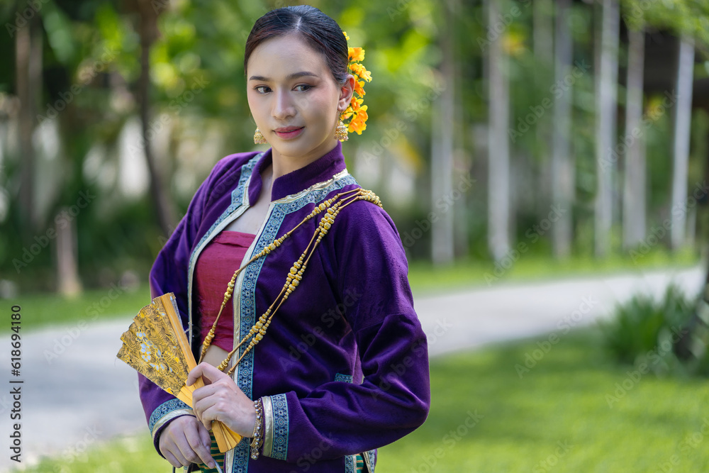 Beautiful pretty young Asian woman wearing a millionaire traditional Thai dress Lanna style standing with an antique silver bag and umbrella in a green natural park. Beautiful pretty young Asian woman wearing a millionaire traditional Thai dress Lanna style standing with an antique silver bag and umbrella in a green natural park.