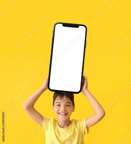 Little boy holding stack of books on yellow background