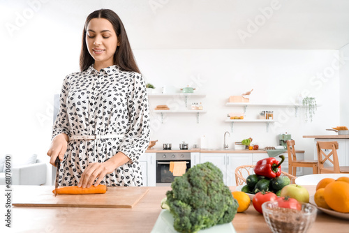 Young woman cutting carrot in kitchen