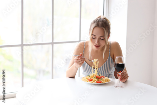 Young woman with glass of wine eating tasty pasta at table in restaurant