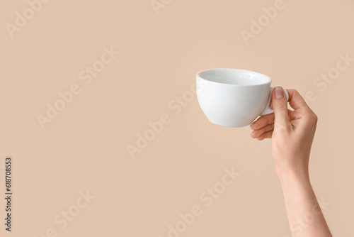 Female hand holding cup on beige background