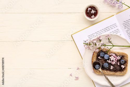 Opened book, plate with sweet jam toast and flowers on white wooden table photo