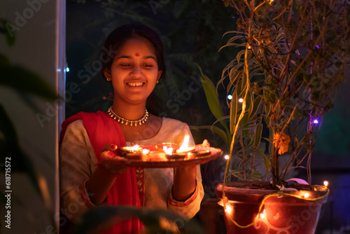 Photography Indian girl posing with plate of diyas in front of camera on Diwali