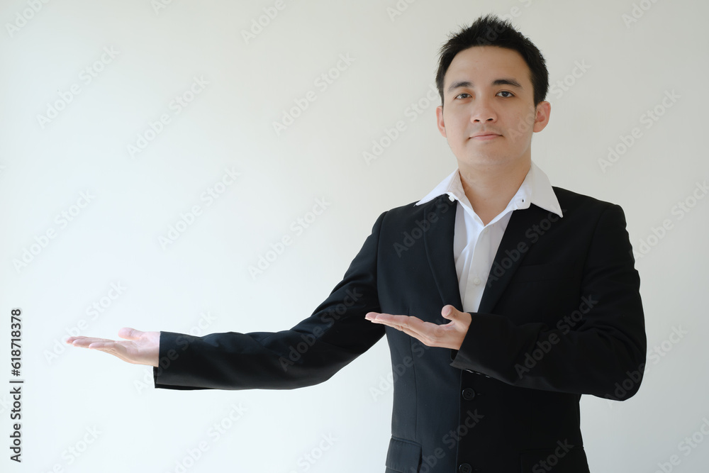 Young Asian businessman opens his both palm hands to his right side and looking to the camera. Isolated white background. Young Asian businessman opens his both palm hands to his right side and looking to the camera. Isolated white background.
