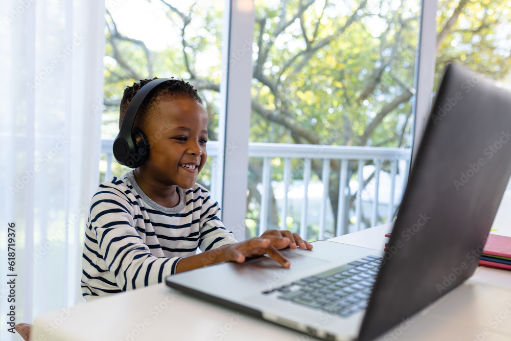 Smiling african american boy wearing headphones and attending online class on laptop at home Smiling african american boy wearing headphones and attending online class on laptop at home