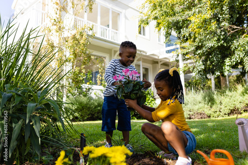 African american boy giving fresh flowers to sister planting in yard outside house