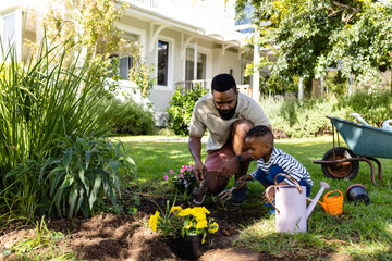 African american father and son digging dirt for planting flowers on field in backyard