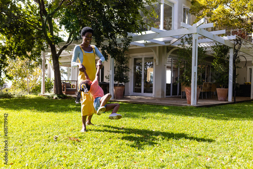 Cheerful african american mother spinning her daughter in backyard outside house