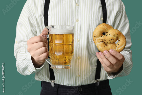Young man in traditional German clothes with beer and pretzel on green background, closeup