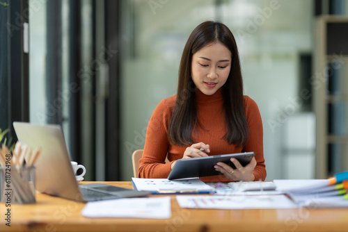 Asian businesswoman using tablet, laptop at modern office to research, record, to make account analysis report, real estate investment data. Division of paperwork. Finance and tax system concept.