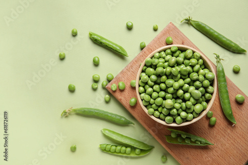 Bowl and wooden board with fresh green peas on color background