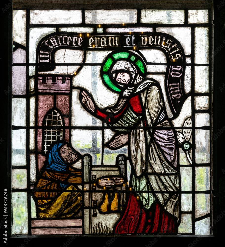 Stained glass church window with scenes of mercy and the lives of saints	