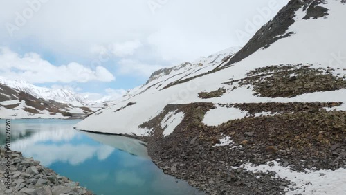 4K shot of beautiful Surajtal Lake surrounded by snow covered mountains from moving vehicle at Lahaul, Himachal Pradesh, India. Turquoise water lake during summer in Indian Himalayas.  photo