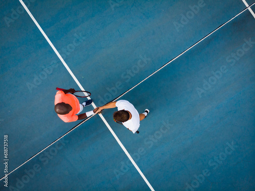 Overhead view of diverse male tennis players shaking hands on outdoor court, copy space