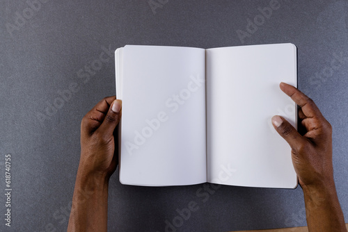 Hands of biracial man holding book with copy space on grey background