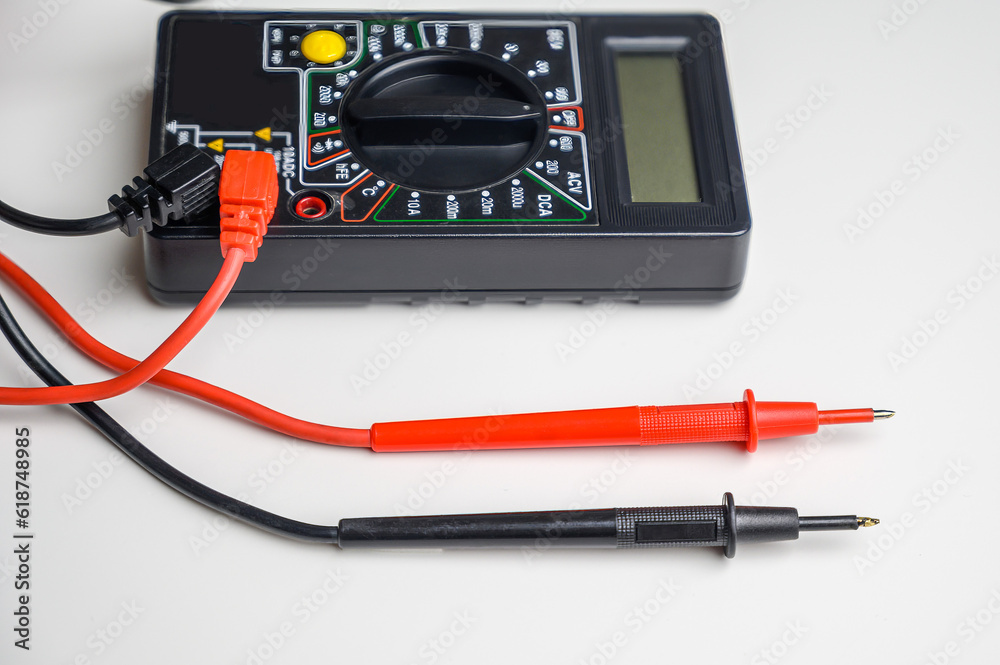 Digital multimeter with test leads on a white table. A multimeter is an electronic measuring instrument. Digital multimeter with test leads on a white table. A multimeter is an electronic measuring instrument.