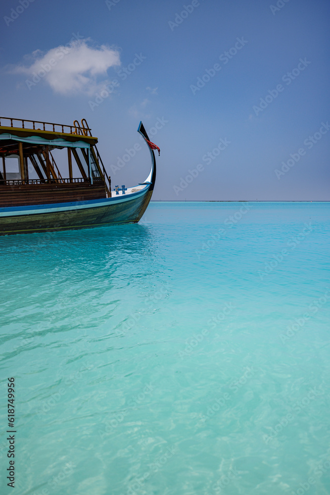 Obraz premium Wooden sailing boat in crystal clear tropical lagoon bay close to beach of deserted exotic island. Maldives Dhoni boat, vertical panorama as luxury travel landscape, amazing vacation wallpaper concept