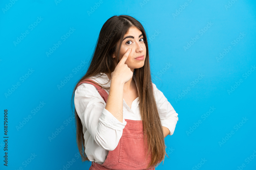 Young caucasian woman isolated on blue background showing something