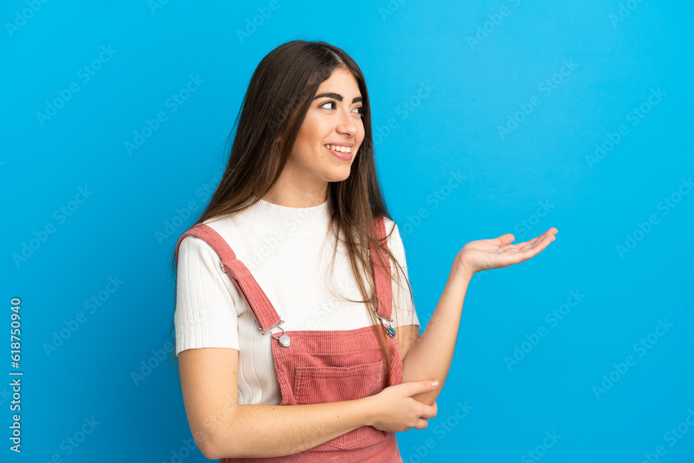 Young caucasian woman isolated on blue background presenting an idea while looking smiling towards