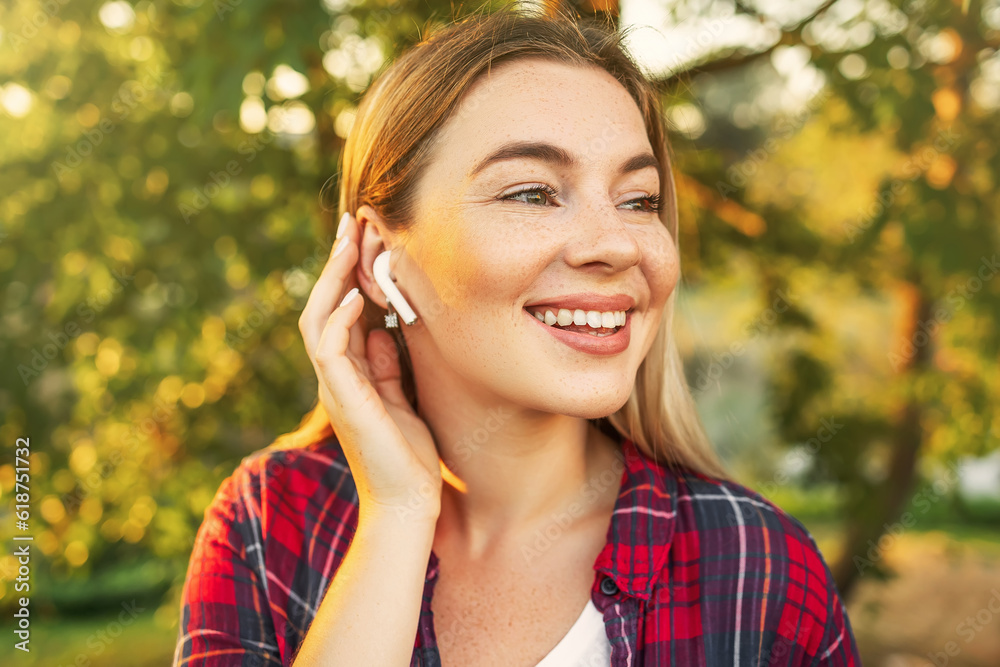 Beautiful girl with with freckles and wireless earphone in the ear on a trees background