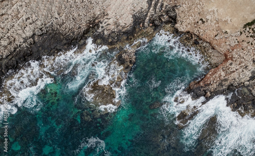 Aerial view of a pristine stretch of crashing waves of the ocean against the rocky shoreline Aerial view of a pristine stretch of crashing waves of the ocean against the rocky shoreline