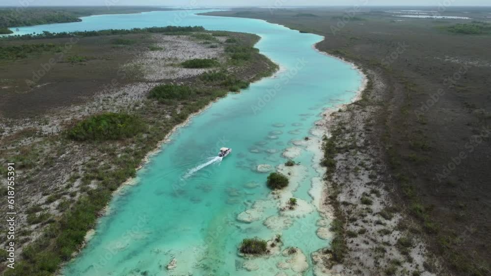 Aerial video of a boat on crystal clear water with green forest on the shore