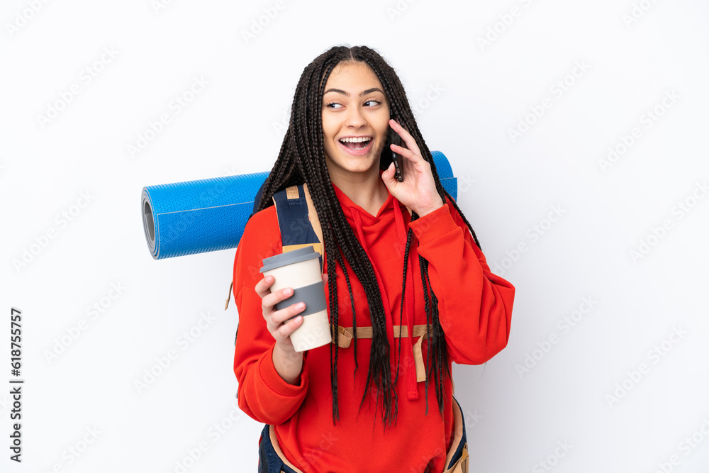 Hiker teenager girl with braids over isolated white background holding coffee to take away and a mobile Hiker teenager girl with braids over isolated white background holding coffee to take away and a mobile