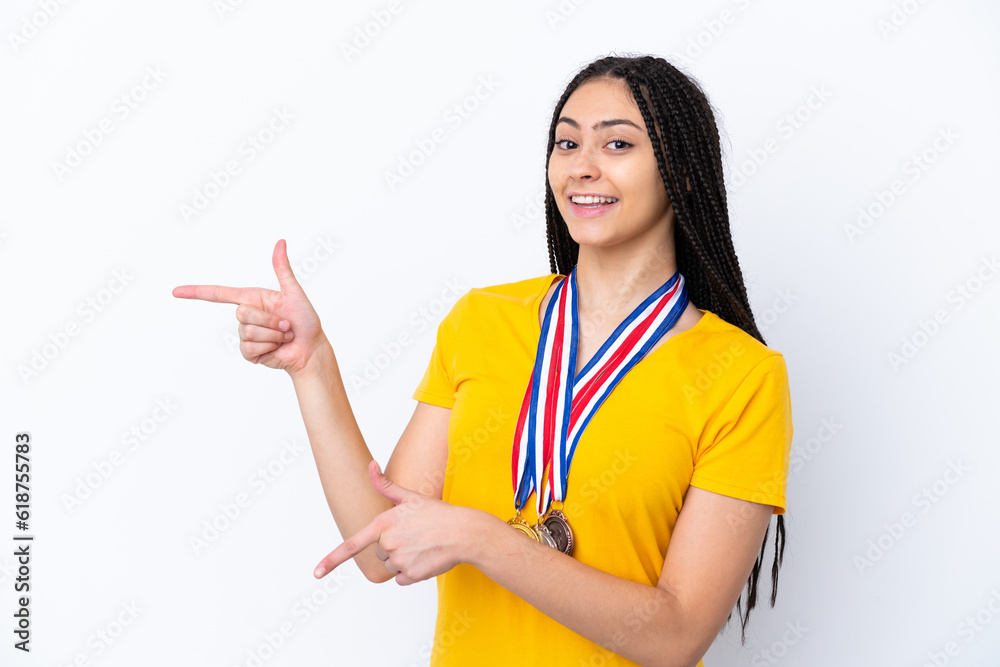 Teenager girl with braids and medals over isolated pink background pointing finger to the side and presenting a product Teenager girl with braids and medals over isolated pink background pointing finger to the side and presenting a product
